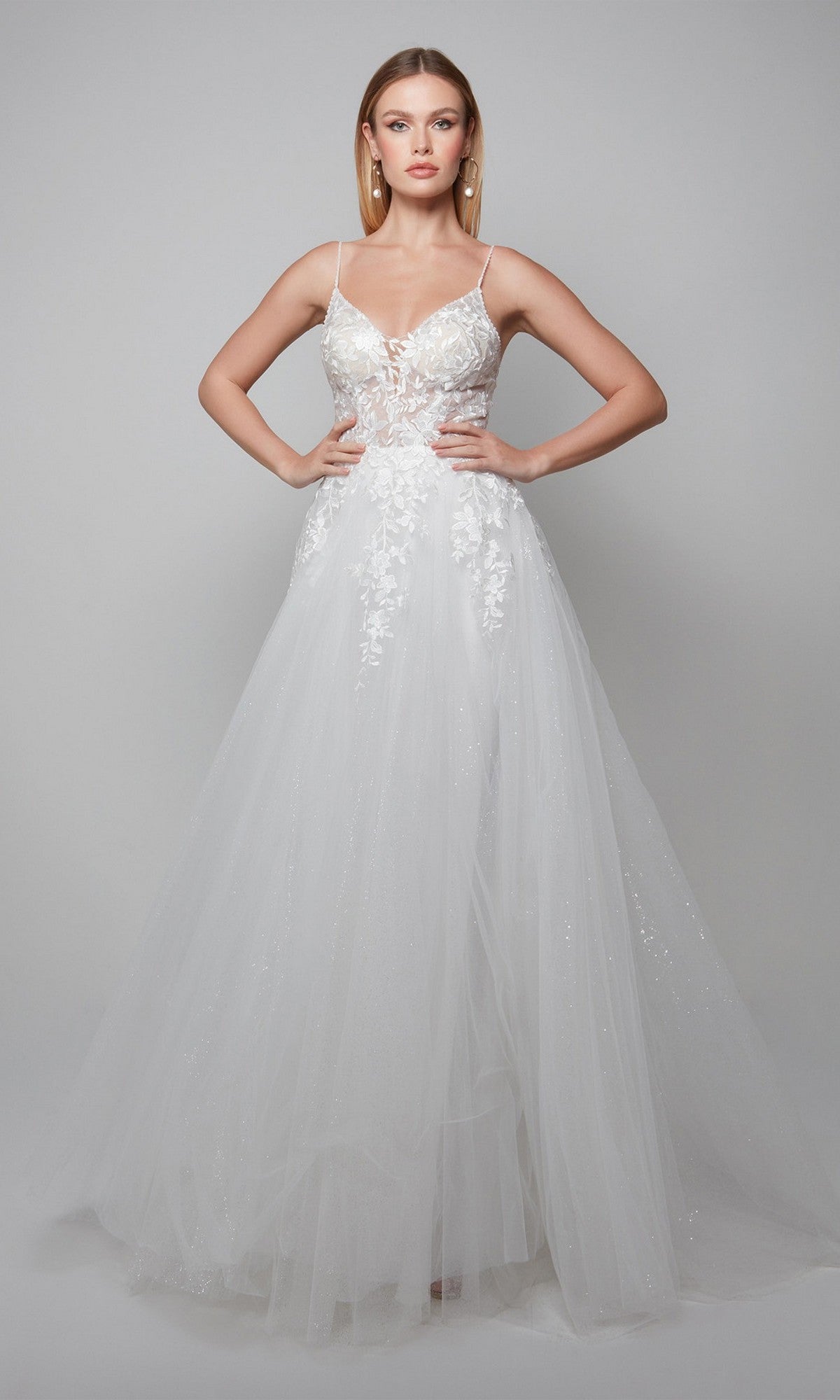 In the Alyce 7079 long ivory dress, featuring a sheer lace-embellished bodice and full tulle skirt, a woman exudes bridal elegance against a plain gray background.
